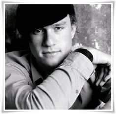 a black and white photo of a man leaning against a wall with his arms crossed