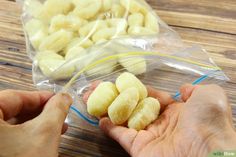 two hands holding small pieces of food in plastic bags on a wooden table next to another person's hand