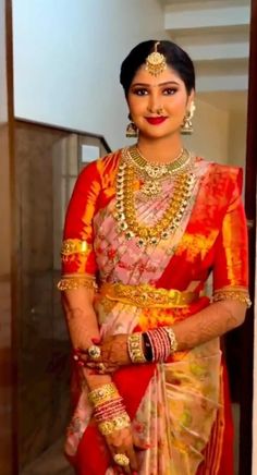 a woman in a red and yellow sari with gold jewelry on her neck, standing next