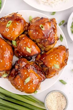 chicken wings covered in sesame seeds and teriyaki sauce on a white plate with green onions