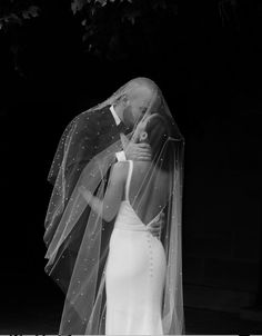 a woman in a wedding dress and veil kissing a man on the forehead with his arm around her