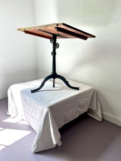 an iron and wood table with a white cloth on the top, in a corner