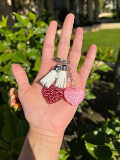 a hand holding two heart shaped keychains in it's palm, with a house in the background