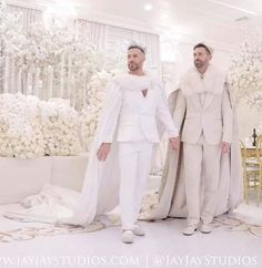 two men standing next to each other in front of a white wedding ceremony backdrop with flowers