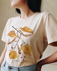 T-shirt featuring a botanical illustration of fall Linden tree (Tilia cordata). Fall in love with our autumn leaves shirt that you won't find anywhere else. Printed on a cream t-shirt, made from durable lightweight cotton. Unisex fit - boxy and long. How it's made: * All prints are original watercolor designs hand-painted by a botanical artist. * Ethically made 100% cotton t-shirts that are made to last. * T-shirts are printed and shipped by my printing partner in the US, Canada, or Europe. * By buying from this shop you are directly supporting a woman-owned small business, created out of love for plants to educate, inspire and keep us connected to the natural world. About the artist: This Shop is an extension of my botanical illustration studio, where I create hand-painted watercolor art White T-shirt With Fall Themed Plant Print, White T-shirt With Plant Print For Fall, Nature-inspired Cotton T-shirt With Screen Print, Botanical Screen Print Cotton T-shirt, Crew Neck Cotton T-shirt With Watercolor Print, Relaxed Fit T-shirt With Plants Print, Nature-inspired Relaxed Fit Short Sleeve T-shirt, Relaxed Fit Nature-inspired Short Sleeve T-shirt, Fall Cotton T-shirt With Plants Print