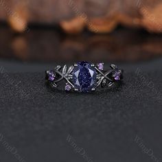 a ring with an oval shaped blue stone surrounded by leaves and purple stones on the side