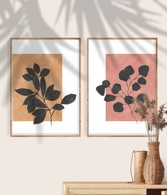 two framed art pieces on a wall above a wooden table with vases and flowers