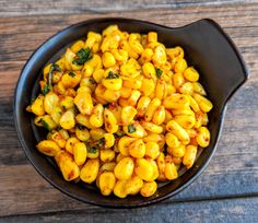 a black bowl filled with corn on top of a wooden table