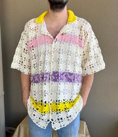 a man wearing a crochet shirt and jeans standing in front of a wall