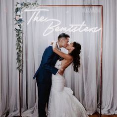 a bride and groom kissing in front of a neon sign