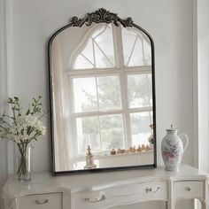 a mirror sitting on top of a white dresser next to a vase with flowers in it