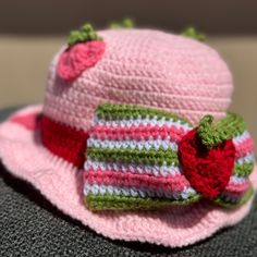 a crocheted hat with a strawberry on the front and green, white, and pink trim