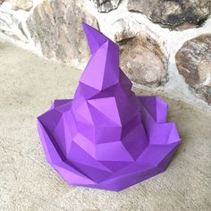 an origami cat sitting on the ground next to a stone wall and rocks