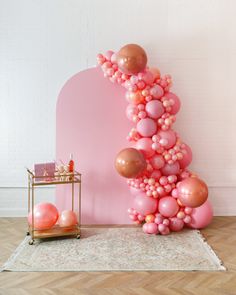 a pink and gold balloon arch next to a table with balloons on the floor in front of it