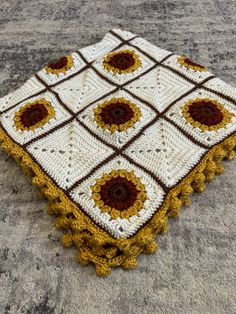 a crocheted square with sunflowers on it sits on the ground in front of a carpet