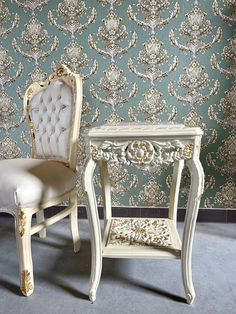 two chairs and a table in front of a wallpapered wall with ornate designs