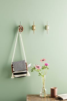 a vase filled with flowers sitting on top of a wooden table next to a wall mounted hook