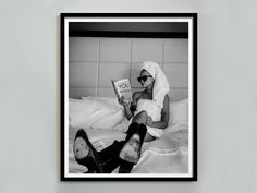 a black and white photo of a woman laying in bed reading a book with her legs crossed