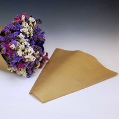 purple and white flowers are in a brown paper bag next to a piece of cardboard