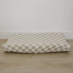 a checkered dog bed on the floor in front of a white wall and wood floor