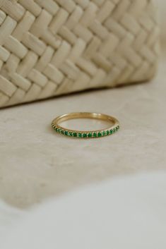 a gold ring with green stones sitting on a white surface next to a woven basket