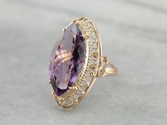 This vintage cocktail ring has lovely filigree details that make it suitable for a marquise cut amethyst. The openwork basket setting lets in plenty of light, while the four sturdy prongs hold even this large stone securely. This particular stone is fantastic! The color is deep true purple, with hints of raspberry, and the size and cut are extraordinary. Metal: 14K Yellow Gold Gem: Amethyst 10.75 Carats Gem Measurements: 23.5 x 11.7 mm, Marquise Cut Ring Size: 7.50 Marks: "14K" Stamped on the in Luxury Gold Marquise Amethyst Ring, Luxury Vintage Amethyst Ring For Formal Occasions, Elegant Marquise Amethyst Ring, Elegant Marquise Amethyst Ring With Prong Setting, Elegant Marquise Cut Amethyst Ring, Elegant Marquise Amethyst Ring For Wedding, Elegant Marquise Amethyst Wedding Ring, Antique Cocktail Ring, Unique Jewelry Vintage