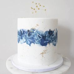 a white cake with blue and gold designs on it sitting on a marble stand next to a wall