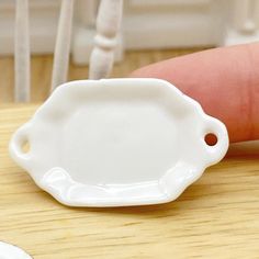 a small white plate sitting on top of a wooden table next to a person's finger