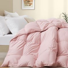 a pink comforter sitting on top of a bed next to pillows and a plant