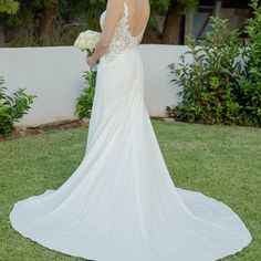 a woman in a wedding dress standing on the grass with her back to the camera