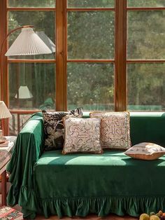 a green couch sitting in front of two windows next to a table with fruit on it