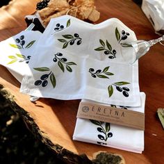 two napkins with an olive design on them sitting on a wooden table next to other items