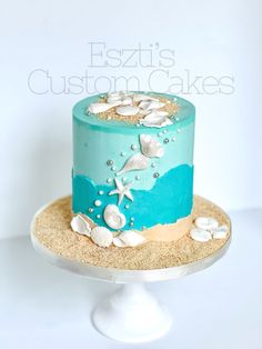 a blue and white cake with seashells on it sitting on a plate in front of a white backdrop