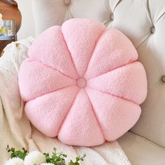 a pink round pillow sitting on top of a white chair next to a vase with flowers