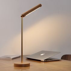 an apple laptop on a wooden table with a gold lamp next to it and a white wall in the background