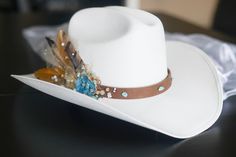 "Bridal Western Cowgirl Hat, ONE SIZE FITS ALL! It is a durable canvas material.  PLEASE NOTE THE BRIDAL VEIL IS NO LONGER AVAILABLE DUE TO LOW DEMAND. If you would like this feature added, please add \"bridal veil\" in the 'message seller' box before purchasing The leather strap has turquoise beads all around it, and on the right side there is a geode blue gem attached to the side, along with champagne (light and dark) colored beading, white beads (sparkly and plain white beading), gold colored tool with glitter embedded in the tool, and 3-4 feathers all attached by gorilla glue and hot glue. The hat also has a vinyl sticker attached to the right side of the hat to let everyone know you are the bride to be! There is an elastic strap on the inside of the hat to keep your head comfortable a Bridal Cowboy Boots, Bridal Cowgirl, Bride Cowgirl Hat, Womens Western Hats, Western Bride, Ivory Bride, Felt Cowboy Hats, Bridal Hat, Bohemian Bridal