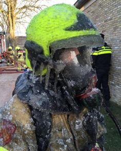 a fireman wearing a green helmet covered in ice and water next to a brick building