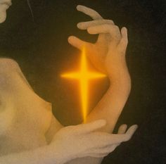 two hands holding a glowing yellow cross in the middle of their palm, against a black background