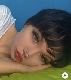 a woman laying on top of a green bed next to a blue wall with piercings