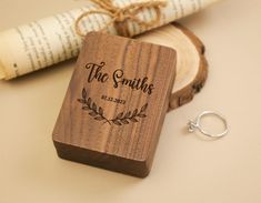 a wooden ring box sitting on top of a table next to an open book and a pair of scissors