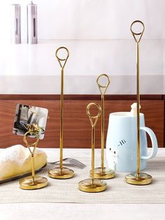 three gold - plated candlestick holders are sitting on a table next to two mugs