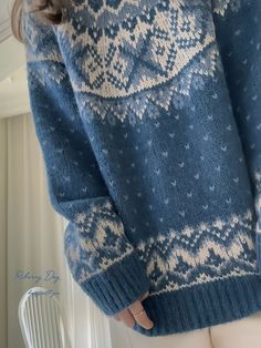 a woman is wearing a blue sweater with white snowflakes on it and has her hands in her pockets