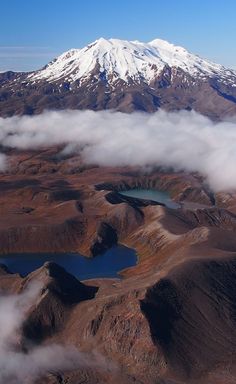 an aerial view of a snow capped mountain and lake in the foreground with low clouds