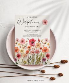 an image of a wedding card on a plate with flowers and pineconis in the background