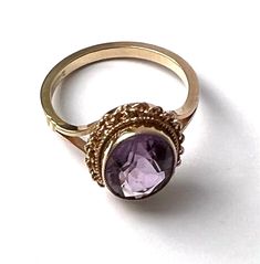 A beautiful solid 9ct gold amethyst dress ring, set with an oval cut amethyst weighing approximately 1.7 carats, bezel set within a rope twist frame with pierced shoulders. A delicate and sophisticated statement ring. The ring has British '375' 9K hallmarks, and the amethyst, light in colour, measures approximately 11 mm by 8 mm.  Stone: Natural amethyst Dimensions: Stone 11 mm x 8 mm Ring size: M Weight: 3 grams We have many other beautiful antique and vintage jewellery on our Etsy store, so pl Oval Amethyst Ring Stamped 14k, Oval Amethyst Ring With Bezel Setting For Formal Occasions, Classic Amethyst Oval Cabochon Ring, Classic Oval Amethyst Ring, Classic Oval Purple Amethyst Ring, Elegant Amethyst Bezel Set Oval Cabochon Ring, Elegant Amethyst Oval Cabochon Ring With Bezel Setting, Gold Amethyst Oval Cabochon Ring, Oval Amethyst Ring With Bezel Setting