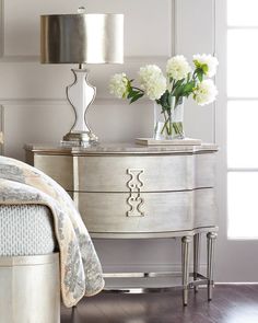 a white dresser sitting next to a bed with flowers on it and a lamp in the corner