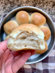 a hand holding a piece of bread in front of a bowl full of buns