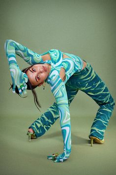 a woman in blue and green pants is doing a dance move with her hands behind her head