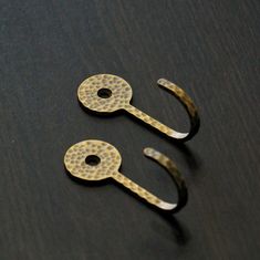 two metal hooks sitting on top of a wooden table next to another pair of scissors