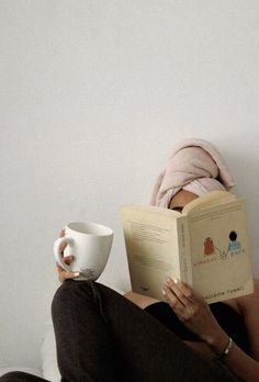 a woman reading a book while holding a coffee cup